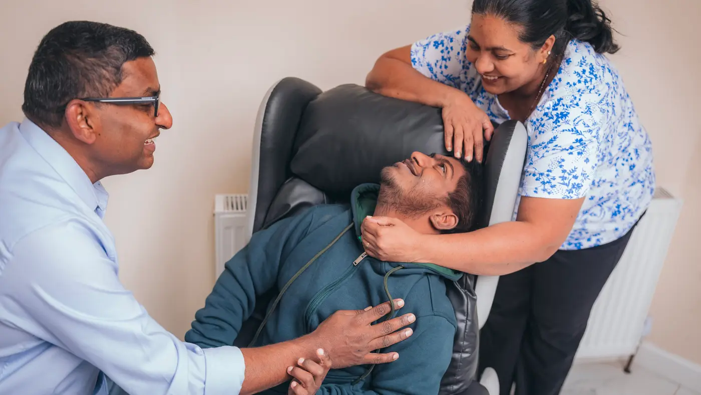 A young man in his chair smiling up at the two people leaning in either side of him